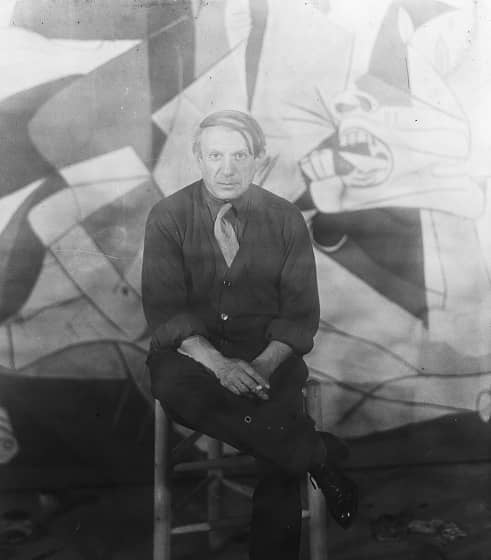 Pablo Picasso sitting in front of Guernica